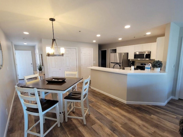 A modern kitchen with white cabinets, a central island, and a dining area with a table and chairs.
