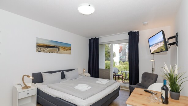 Un dormitorio moderno con cama, mesita de noche, televisión y vistas al exterior.