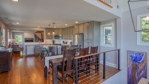 A spacious kitchen with modern appliances, a dining area with wooden chairs, and a view of the outdoors through large windows. - Nautical Soul, Modern Comfort: Canalfront Park Living in Heart of Historic Lewes (Lewes)
