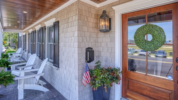 A covered outdoor seating area with Adirondack chairs, a brick wall, a wooden door with a wreath, and an American flag. - Nautical Soul, Modern Comfort: Canalfront Park Living in Heart of Historic Lewes (Lewes)