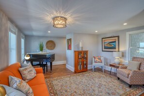 Uma sala de estar com um piano, um tapete estampado e um lustre moderno.