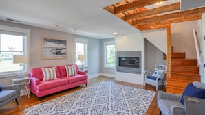 A spacious living room with a red sofa, patterned rug, and a fireplace. - Nautical Soul, Modern Comfort: Canalfront Park Living in Heart of Historic Lewes (Lewes)