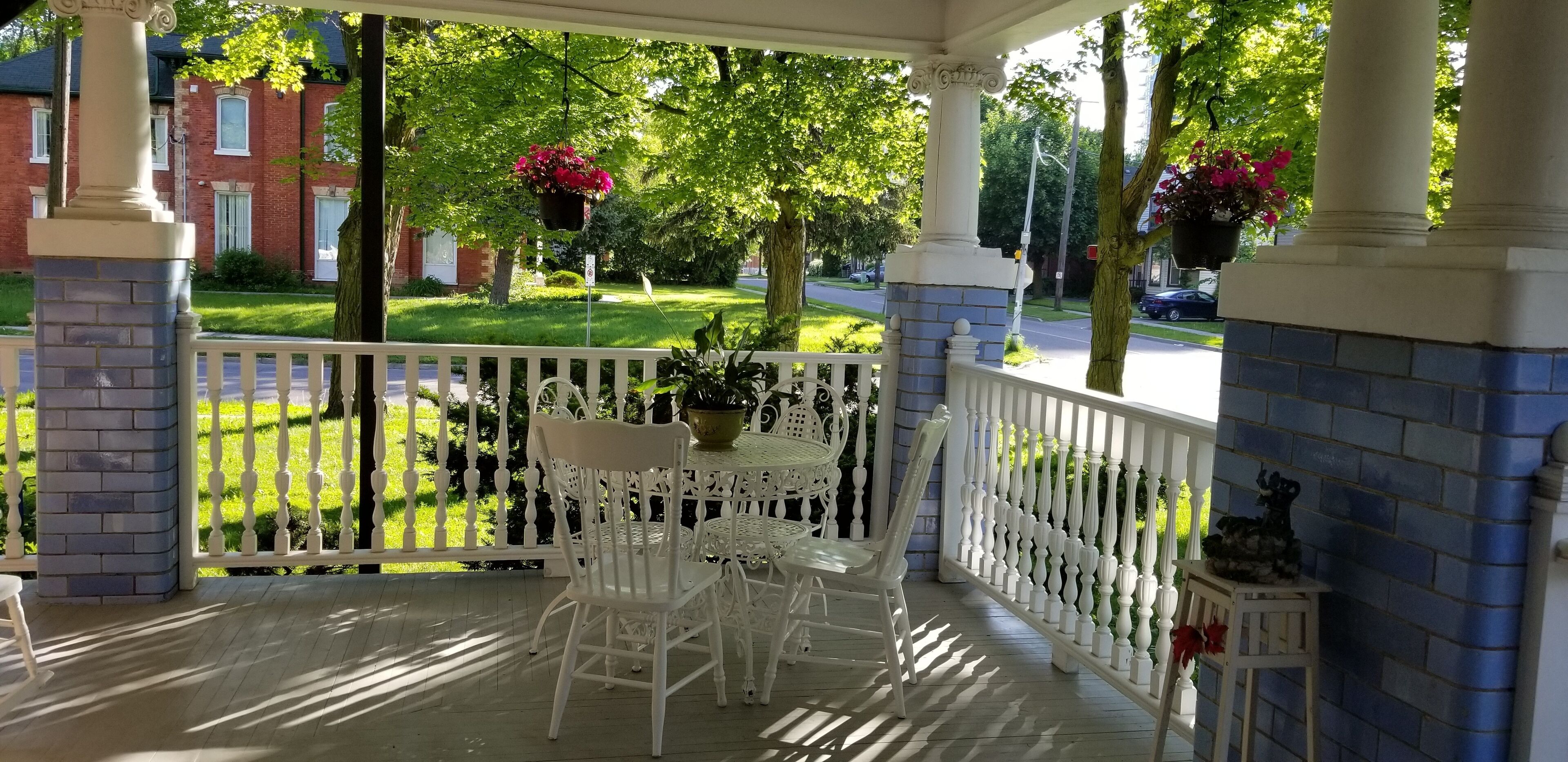 A covered porch with white railings, a table with chairs, and hanging flower baskets.