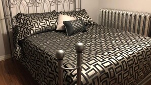 Un lit avec une couvre-lit à motifs géométriques et des coussins assortis, une tête de lit en métal et un radiateur fixé au mur.