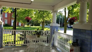 Une véranda couverte avec des balustrades blanches, une table avec des chaises et des jardinières suspendues.