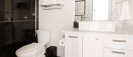 Une salle de bain moderne avec des toilettes, une douche à l’italienne en verre, un lavabo blanc et un miroir.