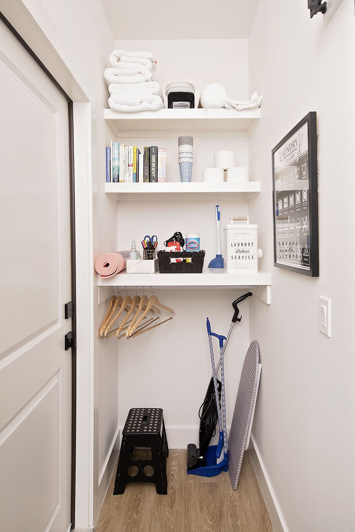 Un cuarto de lavandería con repisas que contienen toallas, libros y productos de limpieza.