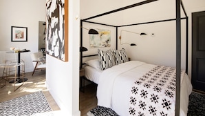 A four-poster bed with a geometric patterned bedspread, a black and white abstract painting on the wall, and a small desk with a chair. - NEW! WhitelineStudio on Ast., Downtown Bentonville new the square (Bentonville)