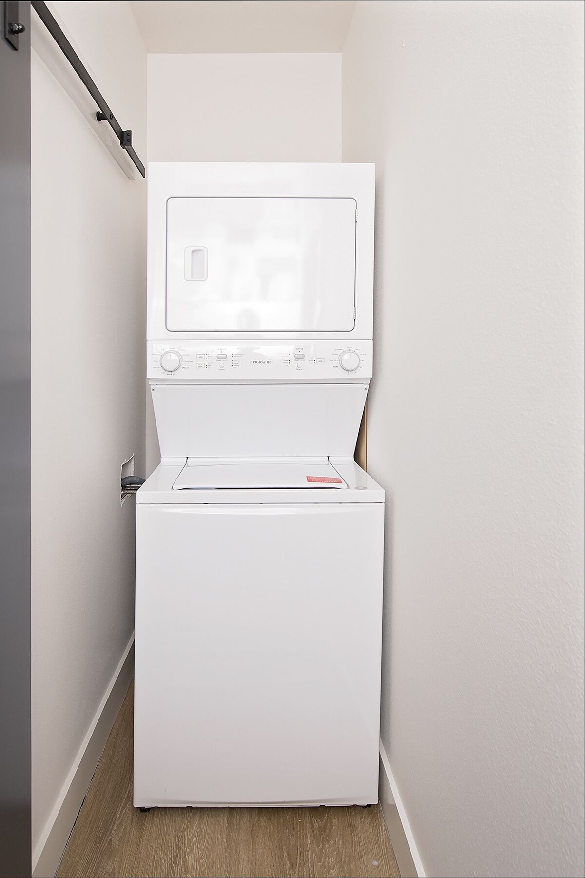 A white front-loading washer and dryer in a narrow hallway with a wooden floor.
