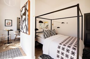 A four-poster bed with a geometric patterned bedspread, a black and white abstract painting on the wall, and a small desk with a chair. - NEW! WhitelineStudio on Ast., Downtown Bentonville new the square (Bentonville)