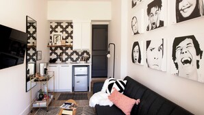 A compact living space with a kitchenette, a black sofa with a white and black pillow, and a wall adorned with black and white artwork. - NEW! WhitelineStudio on Ast., Downtown Bentonville new the square (Bentonville)