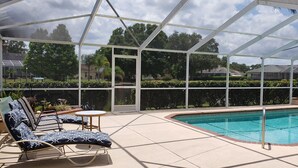 A covered outdoor swimming pool area with lounge chairs and a table, surrounded by a glass enclosure. - Wonderful private Lake house by the canal of lake Arietta (Auburndale)