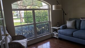 A room with a large window, a blue sofa, a wicker chair, and a small table with a lamp. - Wonderful private Lake house by the canal of lake Arietta (Auburndale)