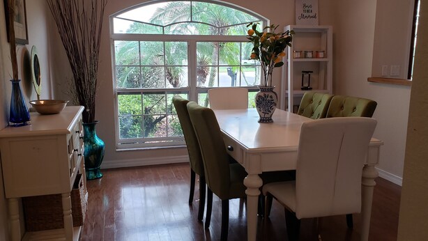 A dining area with a white table, green chairs, and a large window with a view of greenery. - Wonderful private Lake house by the canal of lake Arietta (Auburndale)