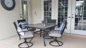 A patio with a table and four chairs, a clock on the wall, and a door with glass panels. - Wonderful private Lake house by the canal of lake Arietta (Auburndale)