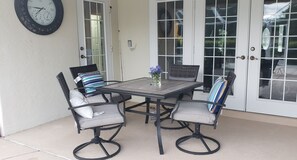 A patio with a table and four chairs, a clock on the wall, and a door with glass panels.