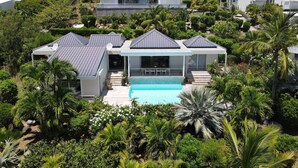 Een resort op een heuvel met meerdere witte villa’s, een zwembad en weelderige tropische begroeiing.