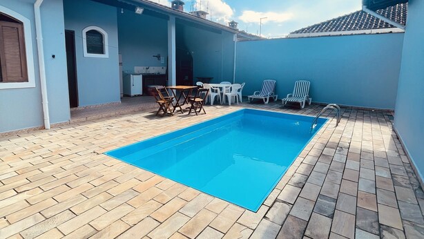 A swimming pool with a tiled deck, a small table, and two chairs. - Vacation home in Peruíbe (Peruibe)