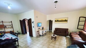 A living room with a dining area, a brown leather sofa, a TV, and a painting on the wall. - Vacation home in Peruíbe (Peruibe)