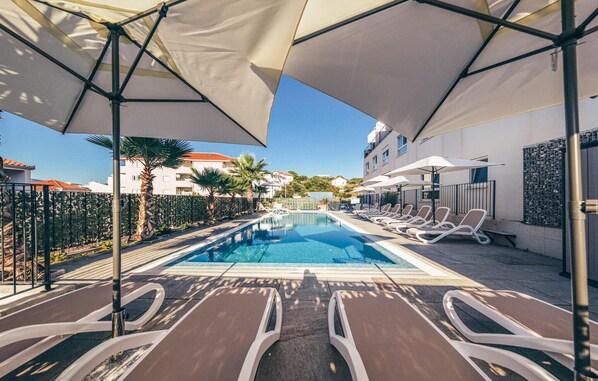 A poolside area with lounge chairs and umbrellas, surrounded by a fence and buildings. - Lovely apartment in Okrug Gornji with heated swimming pool (Okrug Gornji)