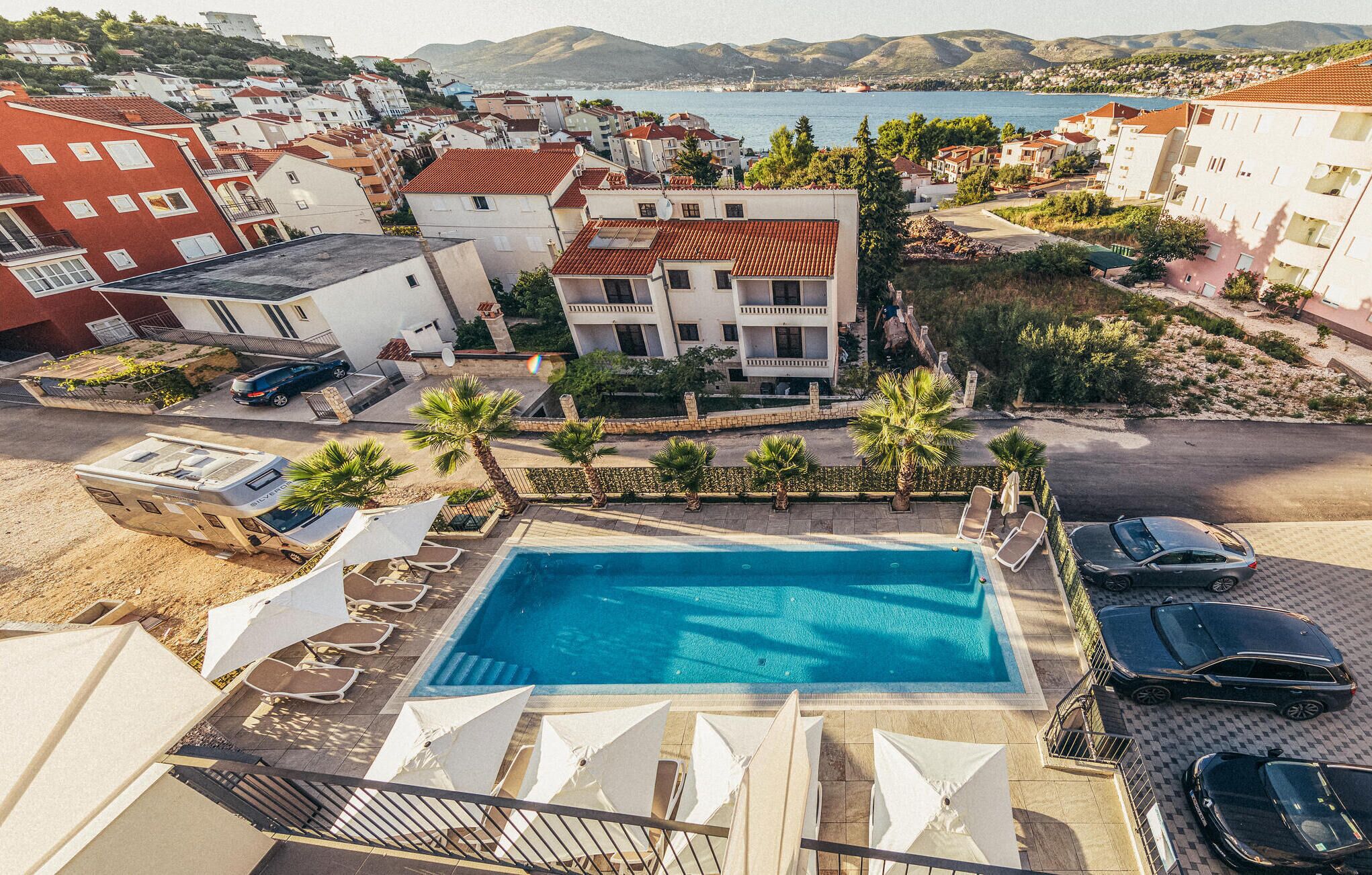 A residential area with a swimming pool, multiple cars, and a view of the sea.