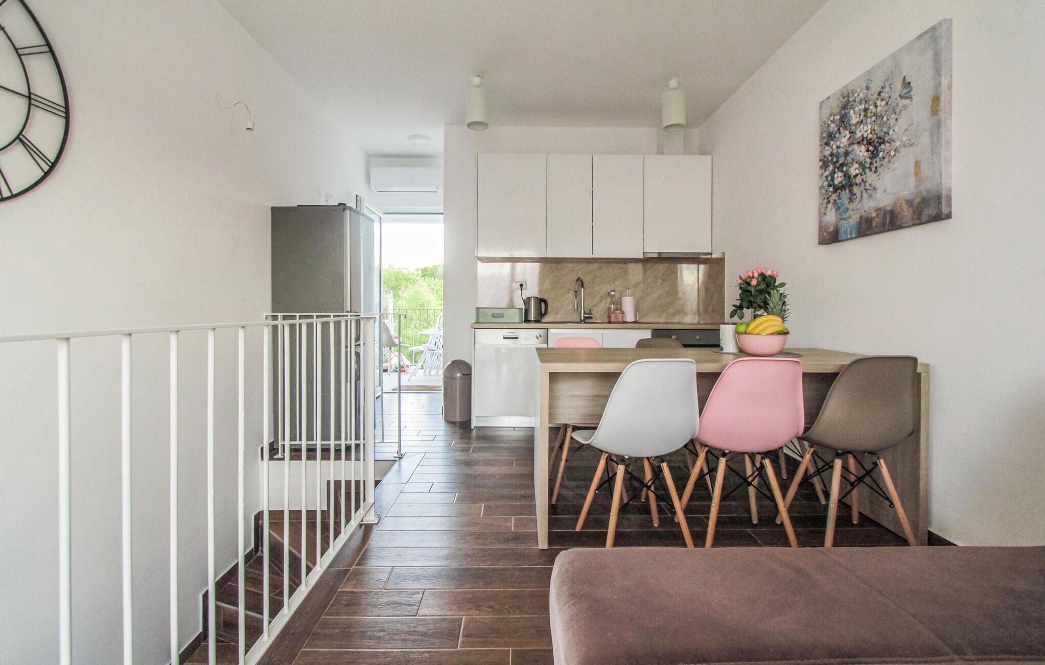 Una cucina moderna con mobili bianchi, un'area pranzo con sedie colorate e una scala che conduce in un'altra stanza.