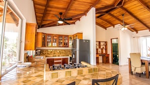 A spacious kitchen with wooden cabinets, a large island with a gas stove, and a ceiling fan. - Flex House – Full Home with Pool and Guest House, Close to the Beach (Esterillos Oeste)