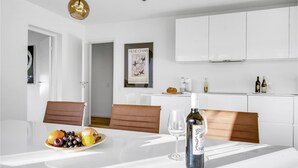 Una zona de menjador moderna amb taula blanca, cadires de cuir, un plat de fruita, una ampolla de vi i una obra d'art emmarcada a la paret.