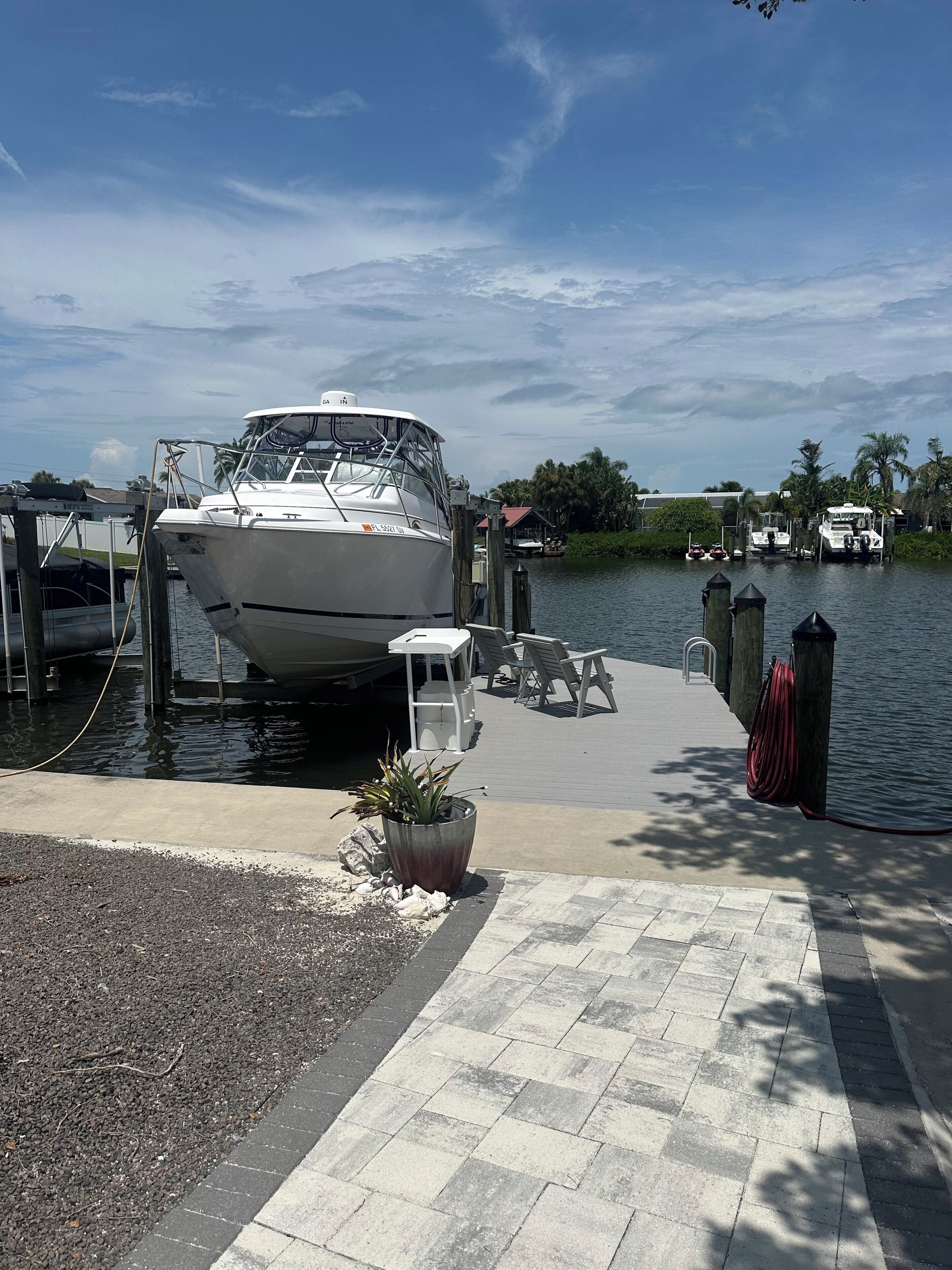 A marina with a docked boat, a paved walkway, and a small potted plant.