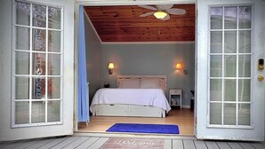 A bedroom with a bed, two wall-mounted lamps, a ceiling fan, and a wooden ceiling. - Adorable Waterfront guest house (Apollo Beach)