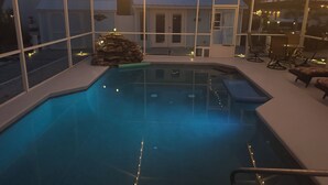 An indoor swimming pool with a stone feature, surrounded by glass walls and string lights. - Adorable Waterfront guest house (Apollo Beach)