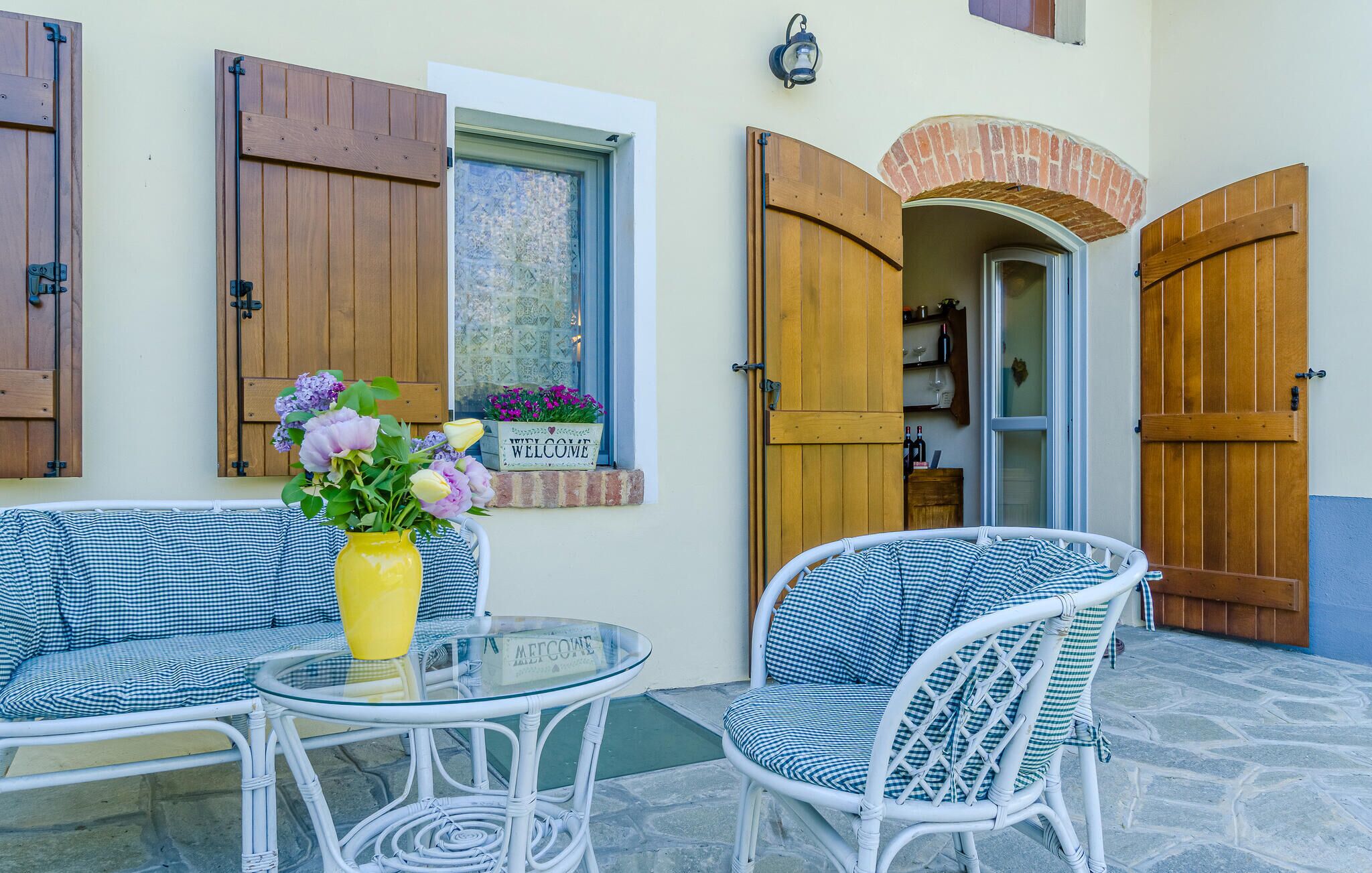 A patio area with wicker furniture, a glass table, and a yellow vase with flowers.