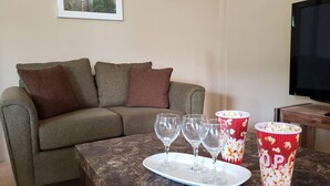 A living room with a sofa, a coffee table with wine glasses and popcorn containers, and a television. - Green Space, Santa Cruz Valley, Trinidad 2 (La Pastora Settlement)
