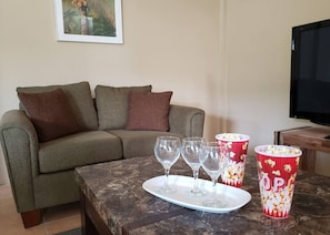 Una sala de estar con un sofá, una mesa baja con copas de vino y recipientes de palomitas, y un televisor.