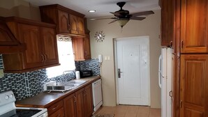 A kitchen with wooden cabinets, a white refrigerator, a stove, a microwave, and a ceiling fan. - Green Space, Santa Cruz Valley, Trinidad 2 (La Pastora Settlement)