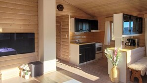 Interior acolhedor de uma cabana com decoração em madeira, lareira, área de cozinha e espaço de estar com mesa de centro e plantas decorativas.