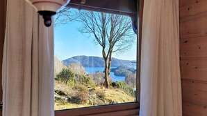 Uma janela com vista para um lago, árvores e colinas.