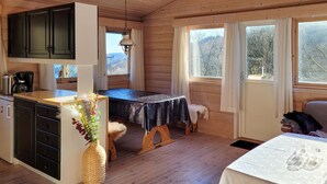 Interior acolhedor de uma cabana com uma mesa de jantar de madeira, uma cozinha com armários, uma cafeteira e um vaso com flores.