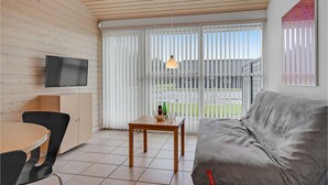 Un salon moderne doté d’un téléviseur à écran plat, d’un canapé gris, d’une table à manger en bois avec des chaises, et d’une porte-fenêtre coulissante donnant sur un espace extérieur.