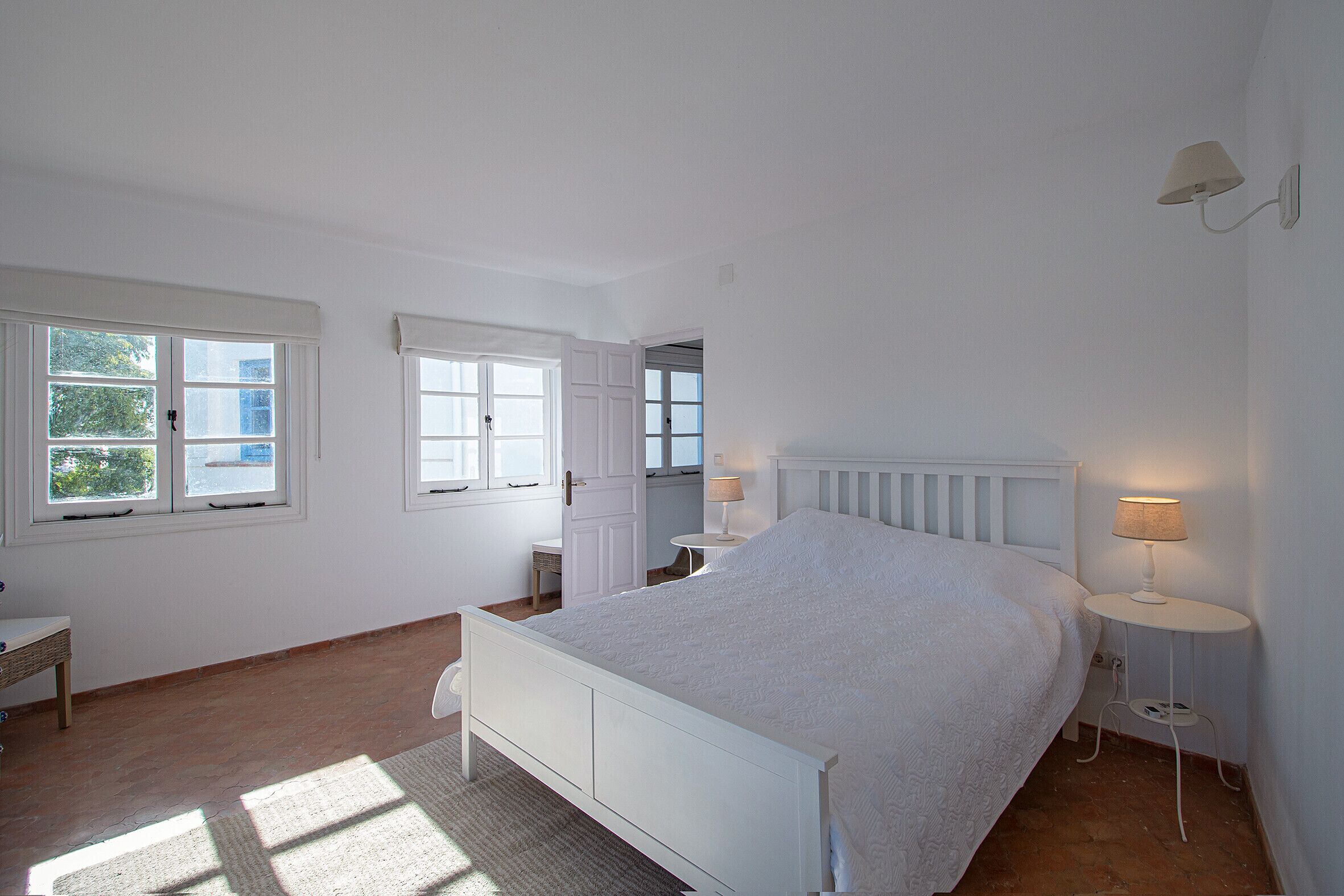 A bedroom with a bed, two bedside tables, a chair, and a window.