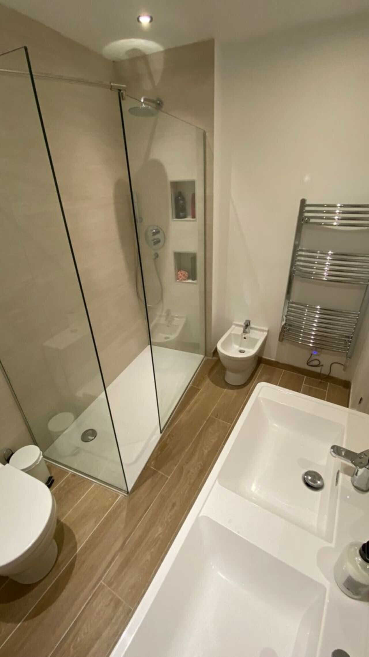 A modern bathroom with a glass shower enclosure, a bidet, a large bathtub, and a towel rack.