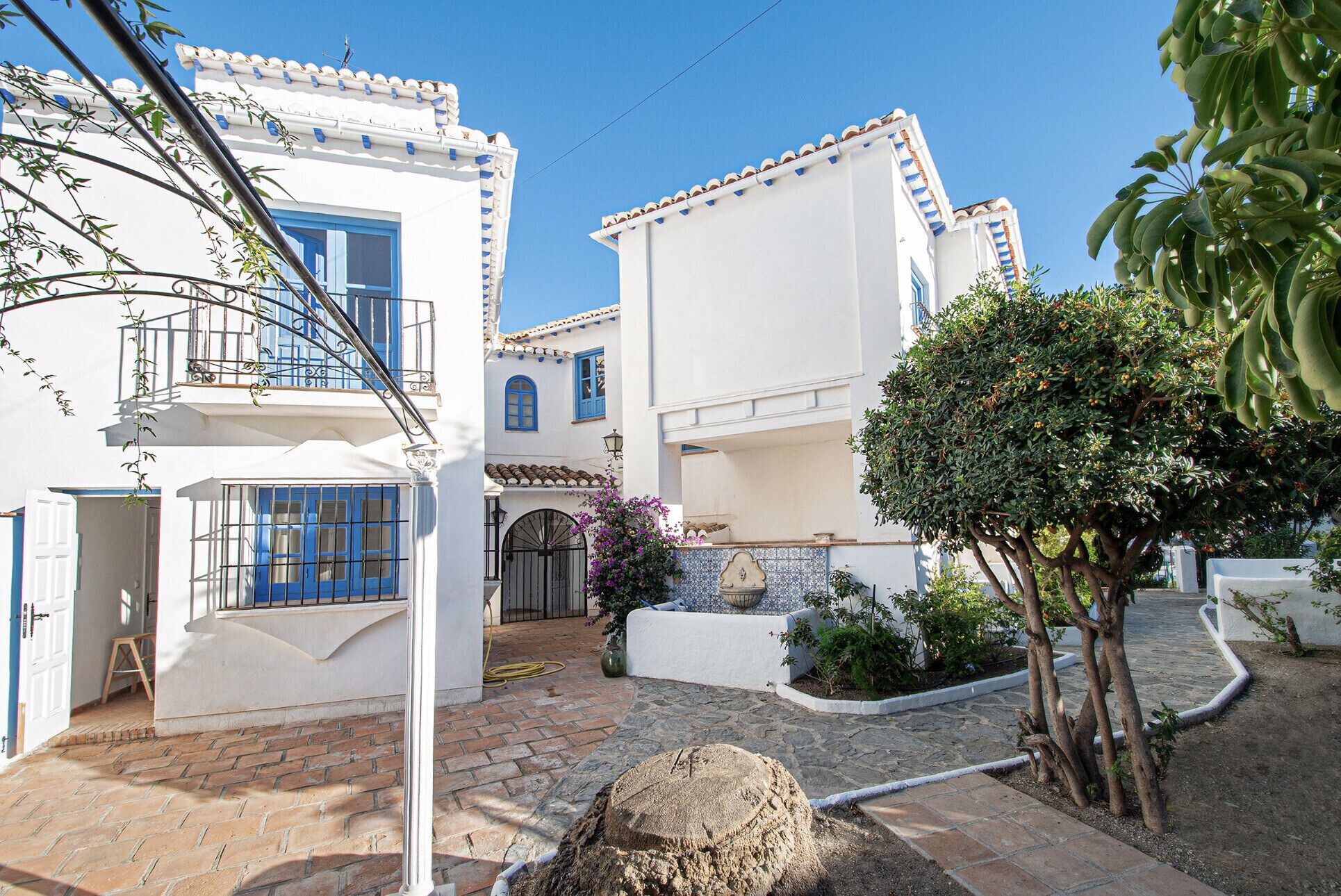 Un edificio de estilo mediterráneo tradicional con patio, paredes blancas, contraventanas azules y entrada empedrada en piedra.