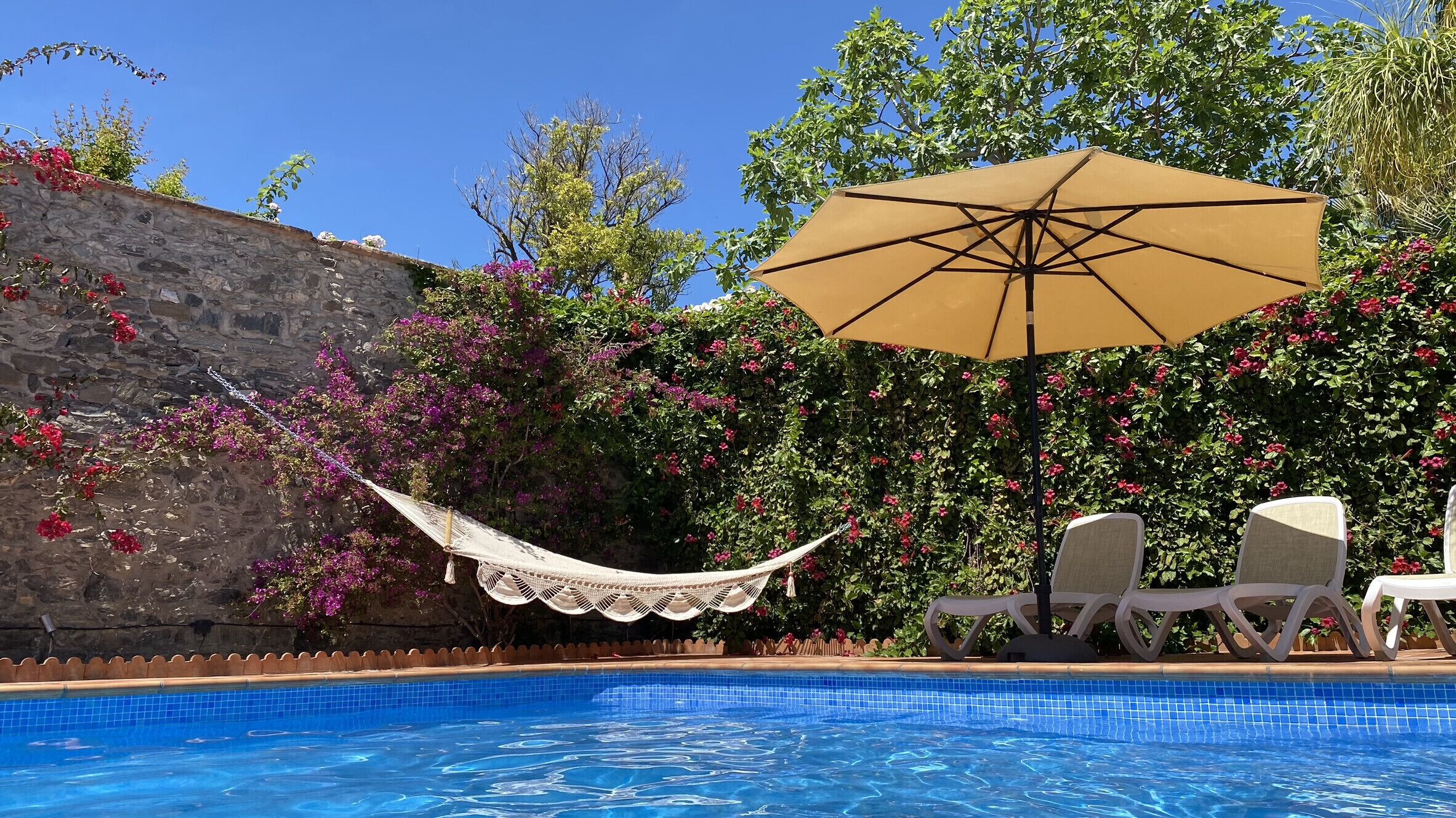 Una piscina con pared de piedra, una hamaca y sillas de descanso.