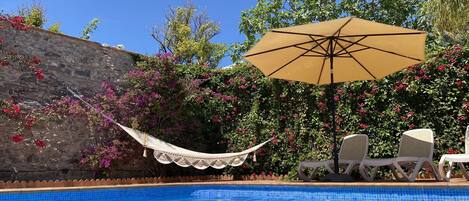 Una piscina con pared de piedra, una hamaca y sillas de descanso.