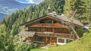 Una cabaña de madera con balcón, rodeada de exuberante vegetación y montañas al fondo.