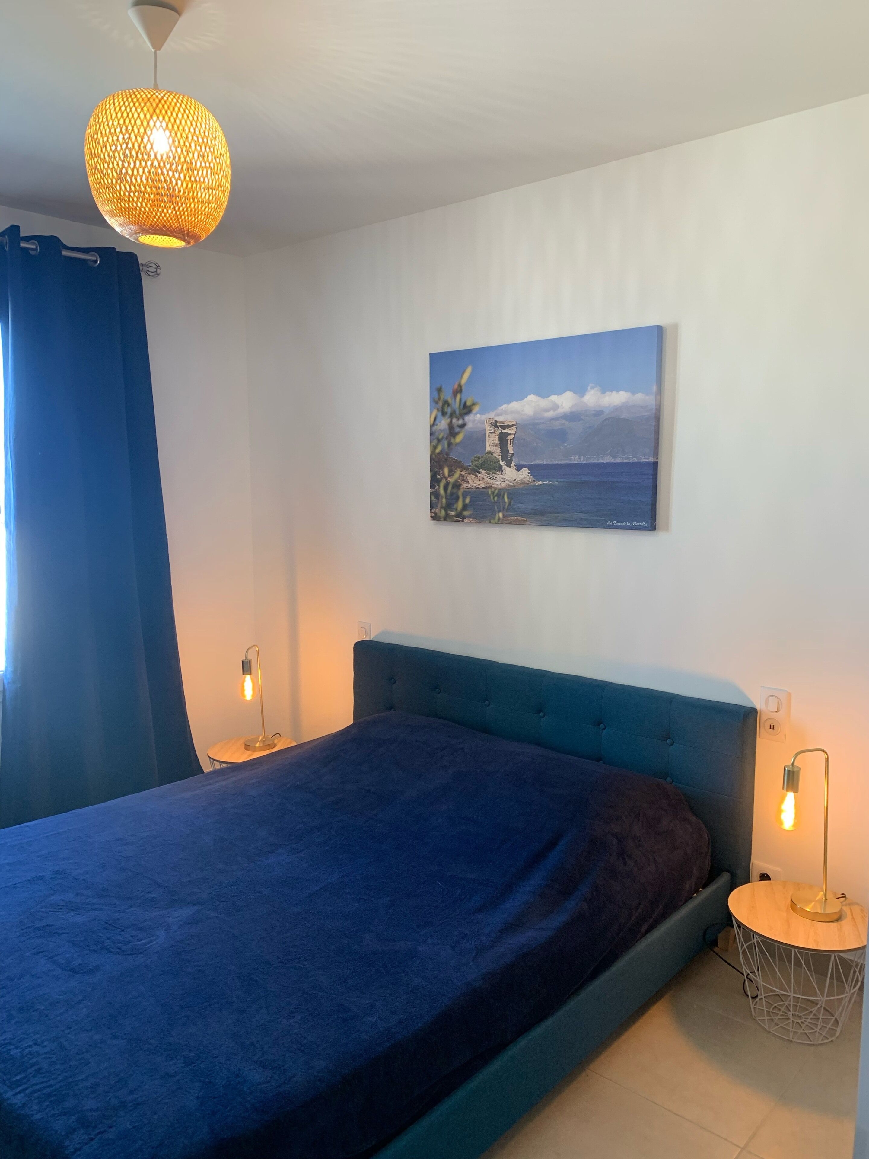Een slaapkamer met een bed, een hanglamp, een aan de muur bevestigd schilderij en bedlampjes.