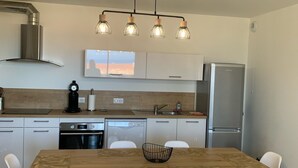 Eine moderne Küche mit Holztisch, weißen Stühlen, integriertem Backofen, Geschirrspüler und Edelstahlkühlschrank.