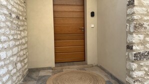 Eine Holztür mit einem Metallgriff, ein kleines schwarzes Objekt an der rechten Wand und eine gewebte Matte auf dem Boden.