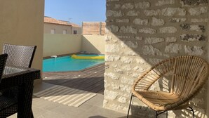 Eine Steinsäule, ein Korbstuhl und ein Pool mit einer gefliesten Terrasse.