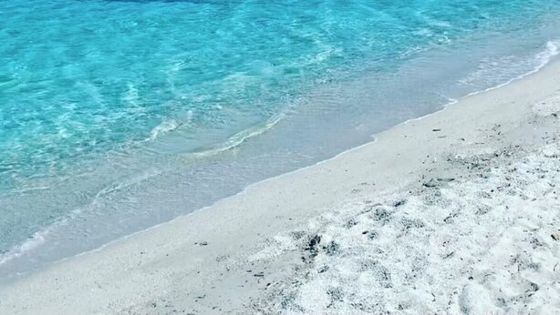Ein Strand mit klarem türkisblauem Wasser und einer bergigen Kulisse.